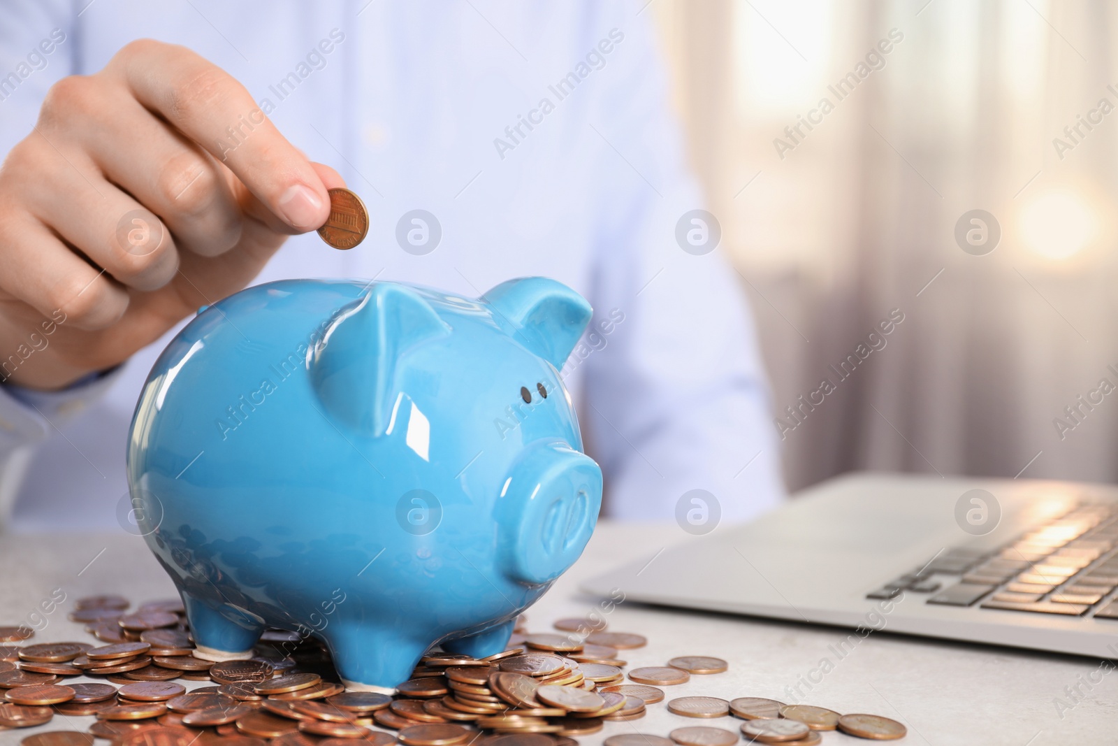 Photo of Man putting coin into piggy bank at table indoors, closeup