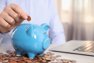 Man putting coin into piggy bank at table indoors, closeup