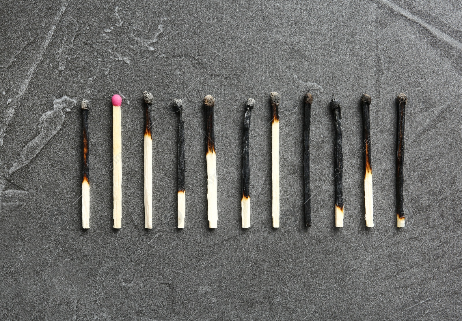 Photo of Row of burnt matches and whole one on grey background, flat lay. Uniqueness concept