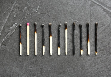 Row of burnt matches and whole one on grey background, flat lay. Uniqueness concept