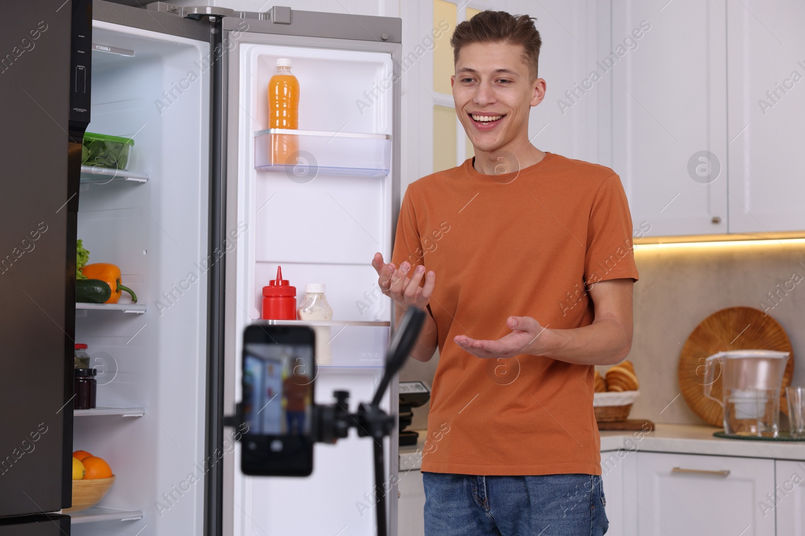 Photo of Smiling food blogger explaining something while recording video in kitchen