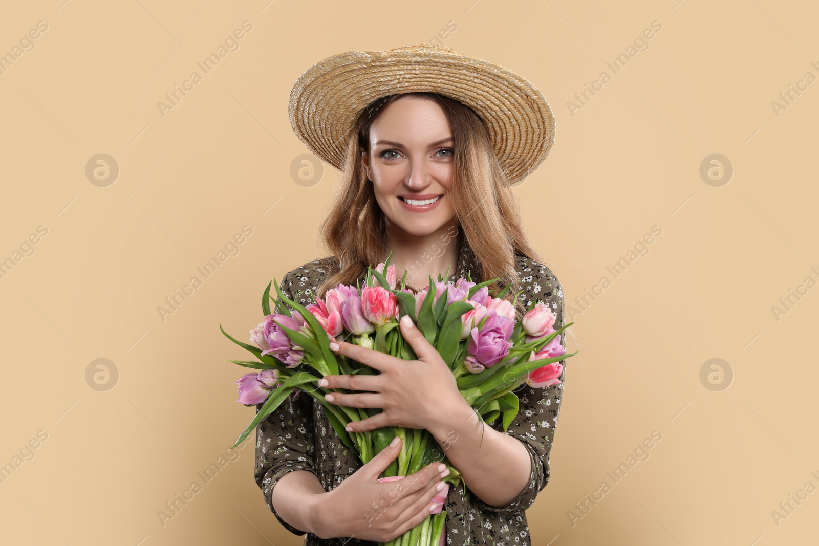 Photo of Happy young woman in straw hat holding bouquet of beautiful tulips on beige background