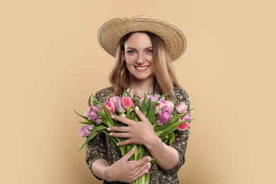 Photo of Happy young woman in straw hat holding bouquet of beautiful tulips on beige background