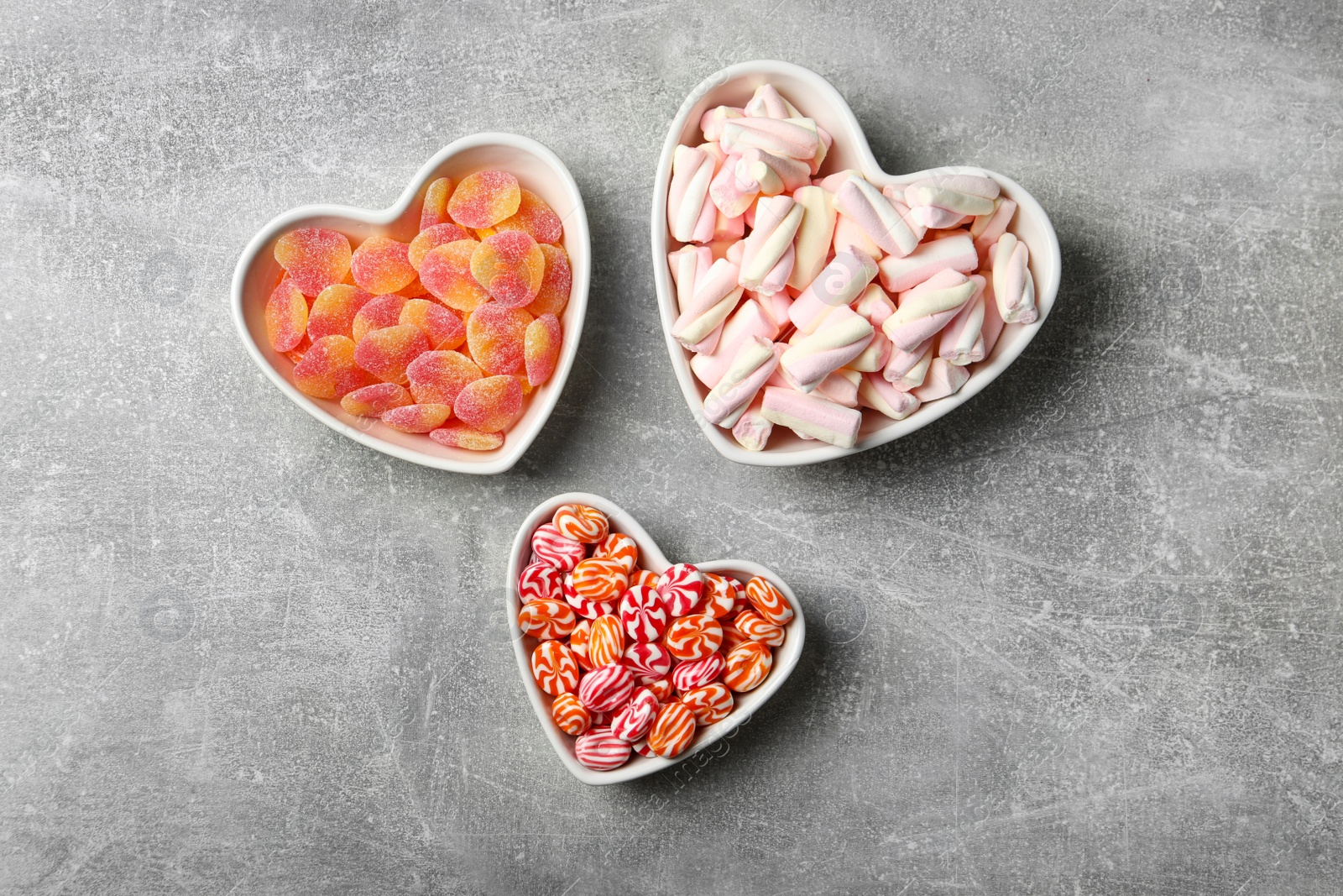 Photo of Tasty sweets in heart shaped bowls on grey table, flat lay