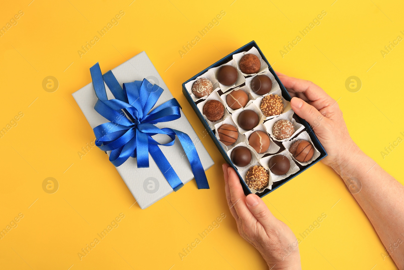 Photo of Woman with box of delicious chocolate candies on yellow background, top view