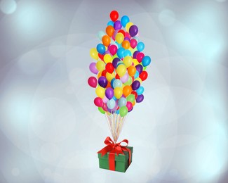 Many balloons tied to gift box on color background