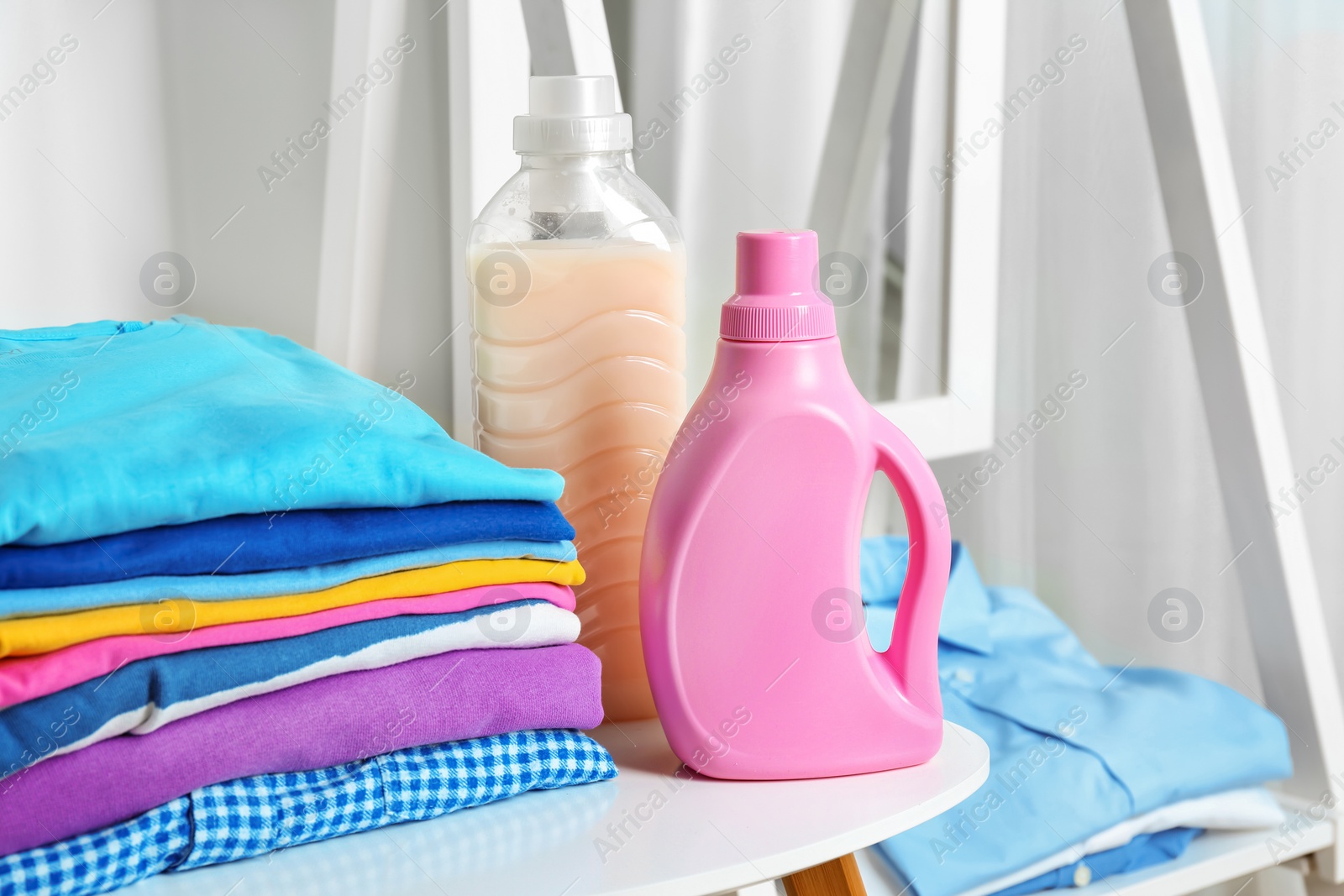 Photo of Stack of clean clothes and bottles with detergent on table