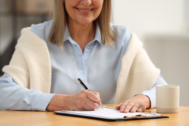 Photo of Smiling senior woman signing Last Will and Testament at table indoors, closeup