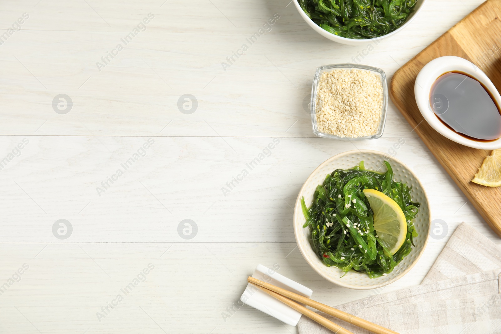 Photo of Japanese seaweed salad with lemon slice served on white wooden table, flat lay. Space for text