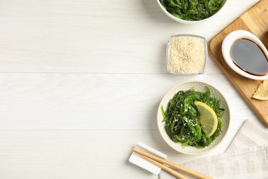 Photo of Japanese seaweed salad with lemon slice served on white wooden table, flat lay. Space for text