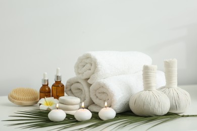 Composition with different spa products, burning candles and plumeria flower on white table