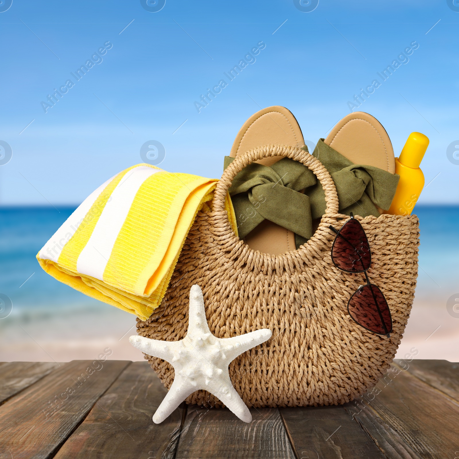 Image of Stylish bag with beach accessories on wooden surface near seashore