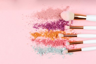 Photo of Makeup brushes and scattered eye shadows on pink background, flat lay. Space for text