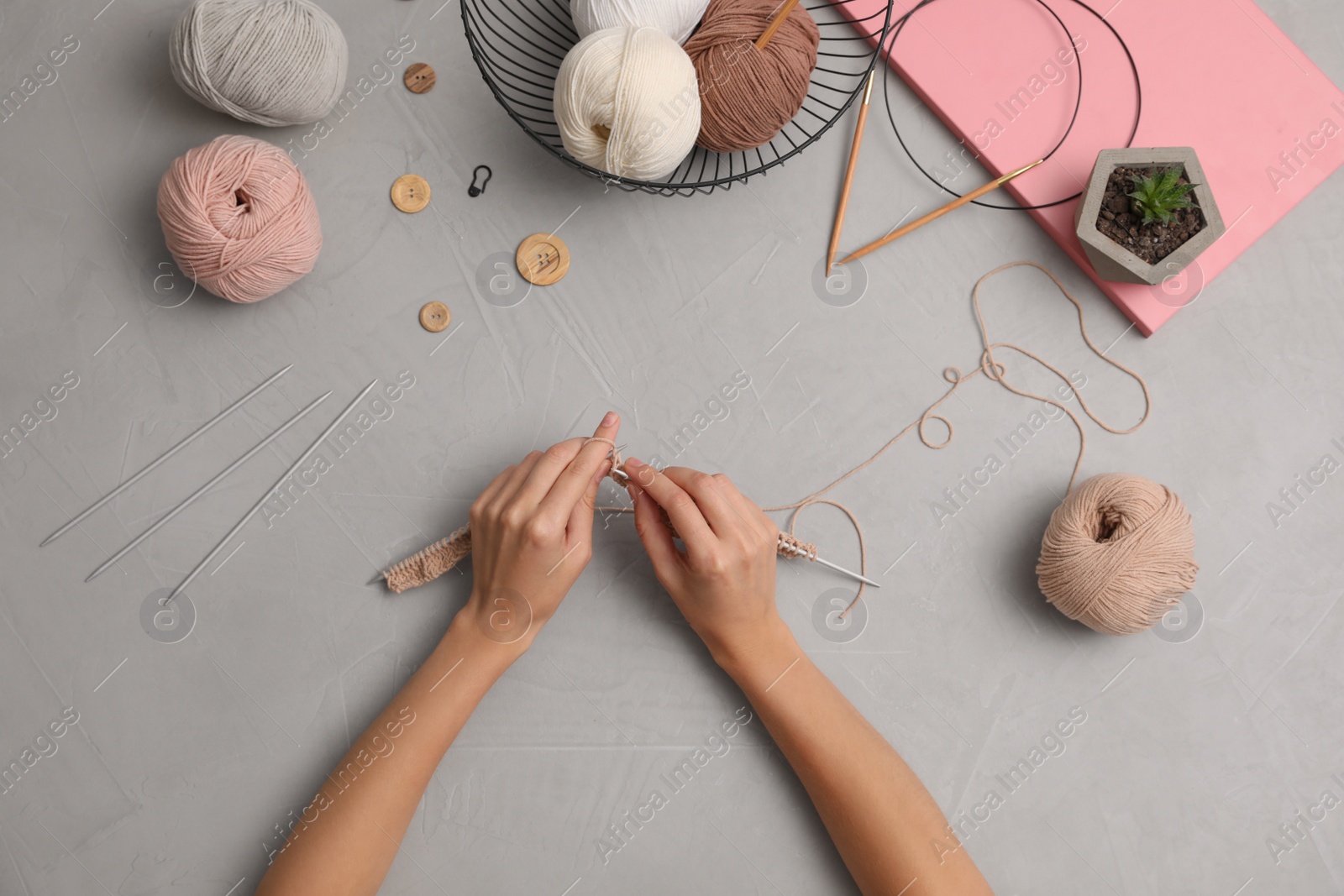 Photo of Woman knitting with threads at grey table, top view. Engaging hobby