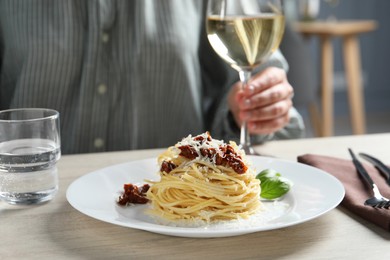 Woman enjoying tasty spaghetti with sun-dried tomatoes and parmesan cheese and wine at wooden table in restaurant, closeup. Exquisite presentation of pasta dish