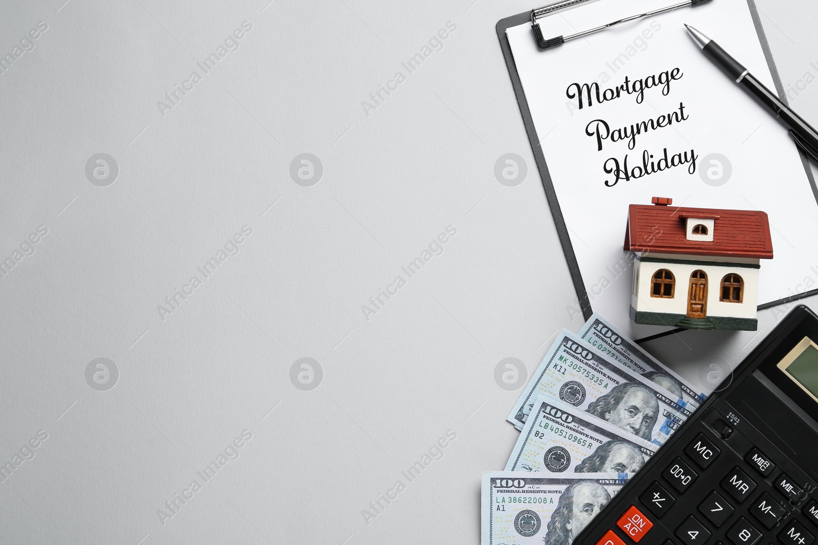 Photo of Clipboard with words Mortgage Payment Holiday, house model, calculator and money on grey background, flat lay. Space for text