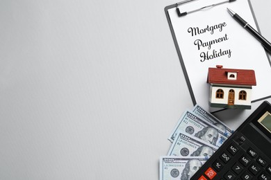 Photo of Clipboard with words Mortgage Payment Holiday, house model, calculator and money on grey background, flat lay. Space for text