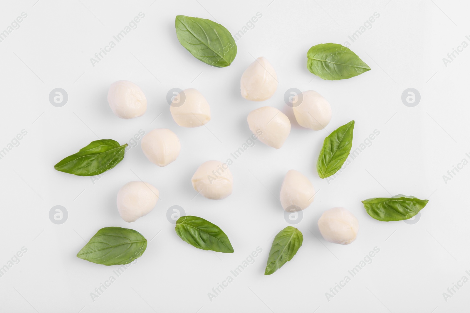 Photo of Tasty mozzarella balls and basil leaves on white background, flat lay