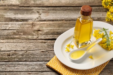 Photo of Rapeseed oil in glass bottle, gravy boat and beautiful yellow flowers on wooden table, space for text