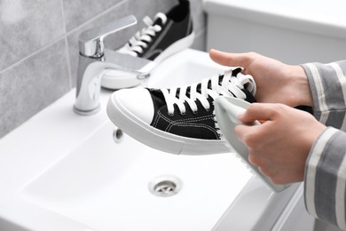 Woman washing stylish sneakers with brush in sink, closeup