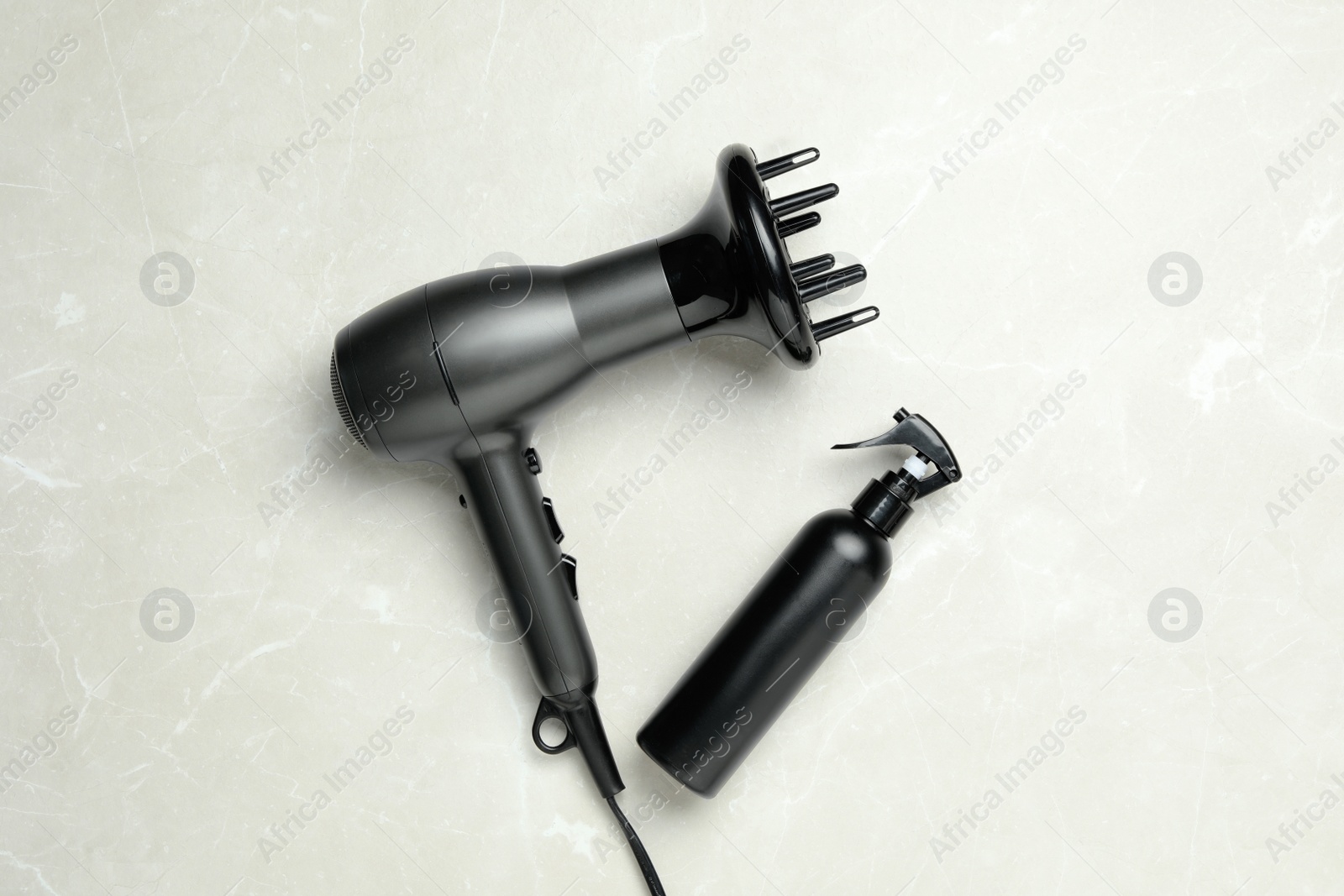 Photo of Hair dryer and bottle on light marble table, flat lay. Professional hairdresser tool