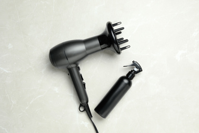 Hair dryer and bottle on light marble table, flat lay. Professional hairdresser tool