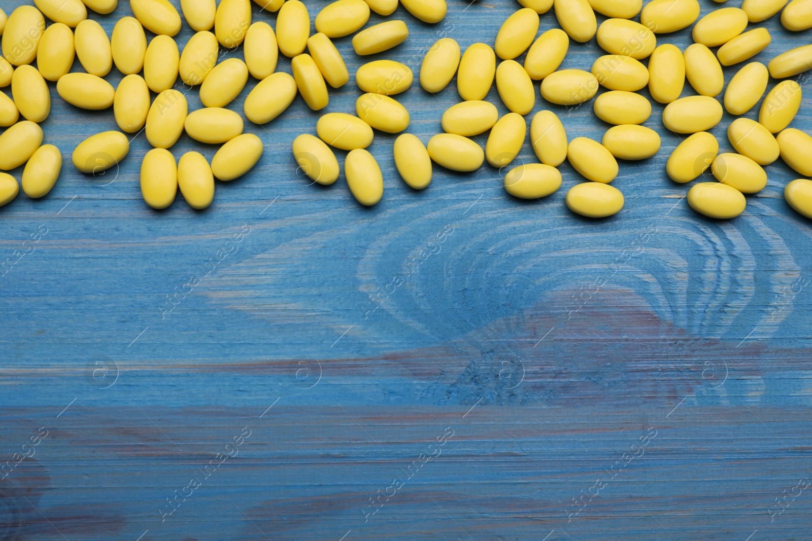 Photo of Many tasty dragee candies on blue wooden table, flat lay. Space for text