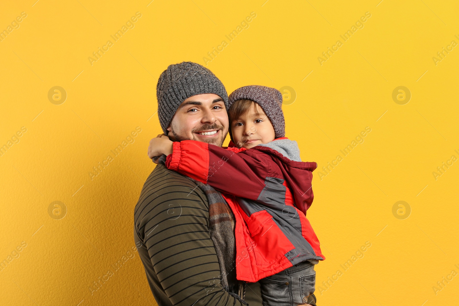 Photo of Happy father and son in warm clothes on yellow background. Winter vacation