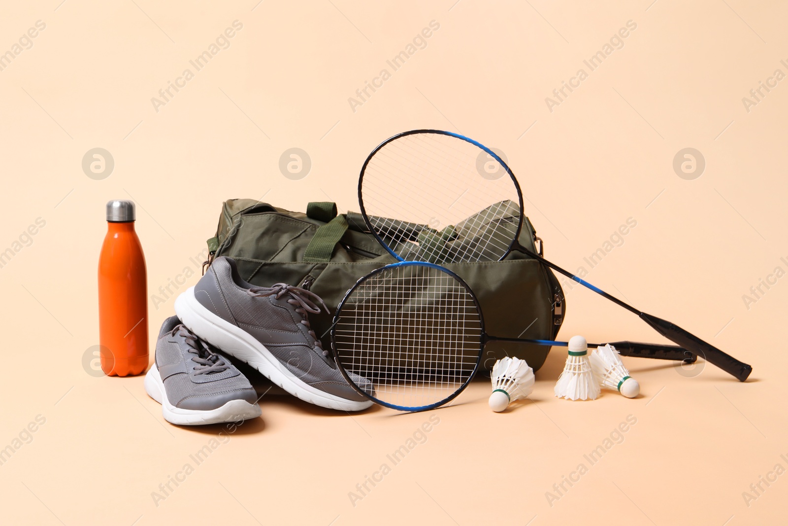 Photo of Badminton set, bag, sneakers and bottle on beige background