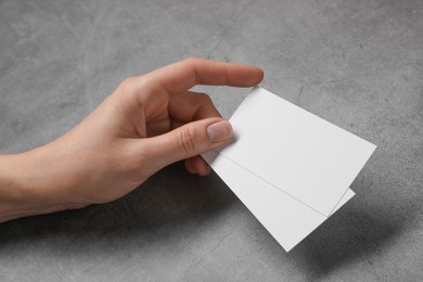 Woman holding blank cards at grey table, closeup. Mockup for design