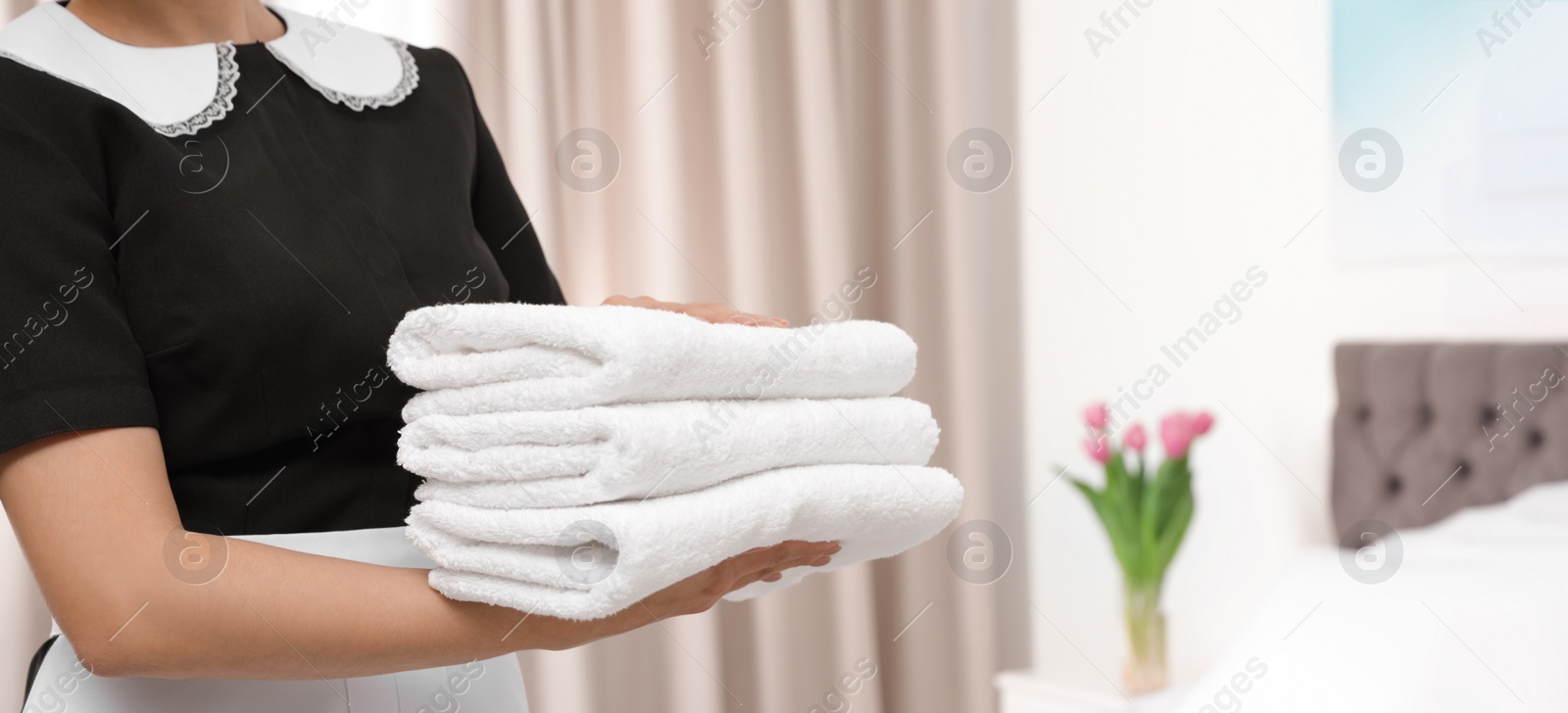 Image of Young maid holding stack of fresh towels in hotel room, closeup view with space for text. Banner design