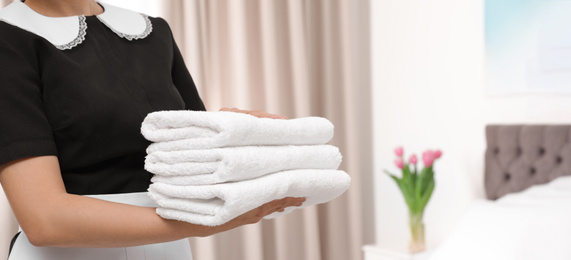 Image of Young maid holding stack of fresh towels in hotel room, closeup view with space for text. Banner design