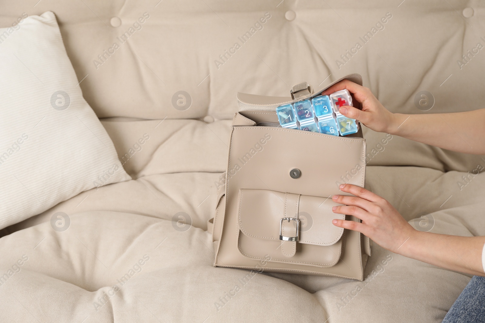 Photo of Woman putting pill box into backpack on sofa, closeup