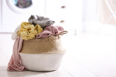 Photo of Wicker basket with dirty laundry on floor indoors, space for text