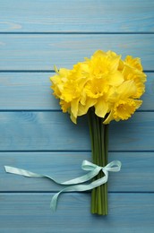 Photo of Beautiful daffodil bouquet on blue wooden table, top view