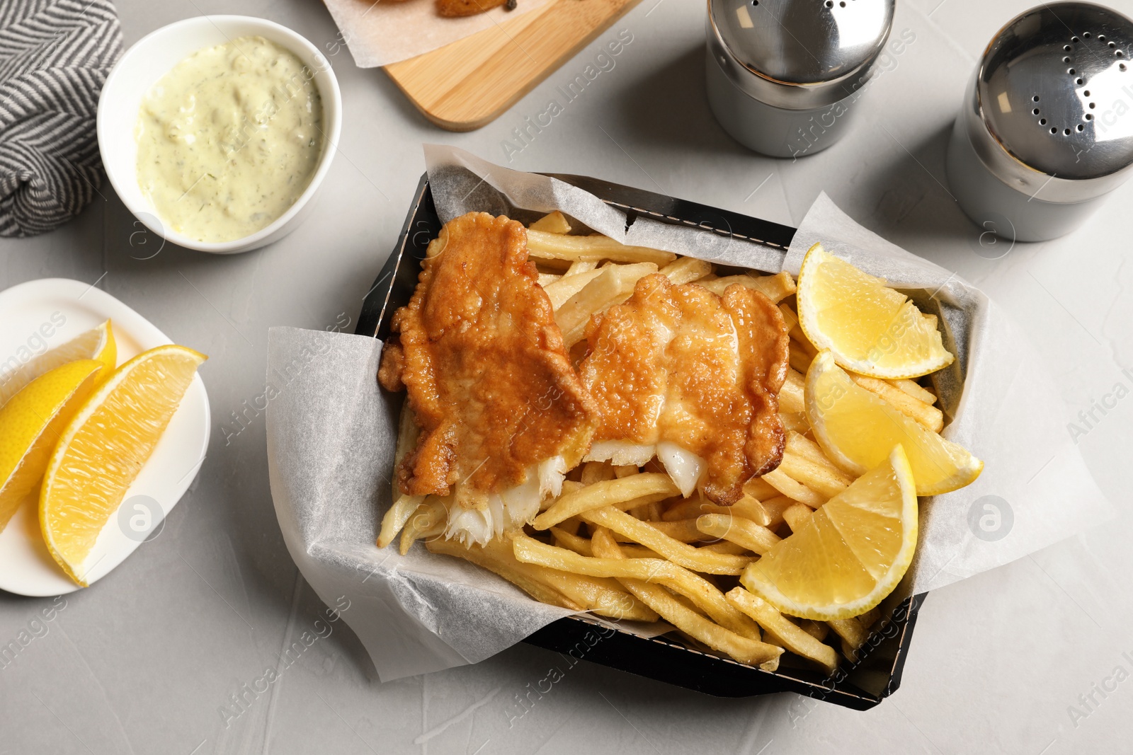 Photo of Container with British traditional fish and potato chips on light background, top view