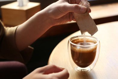 Photo of Woman adding sugar to aromatic coffee at table in cafe, closeup