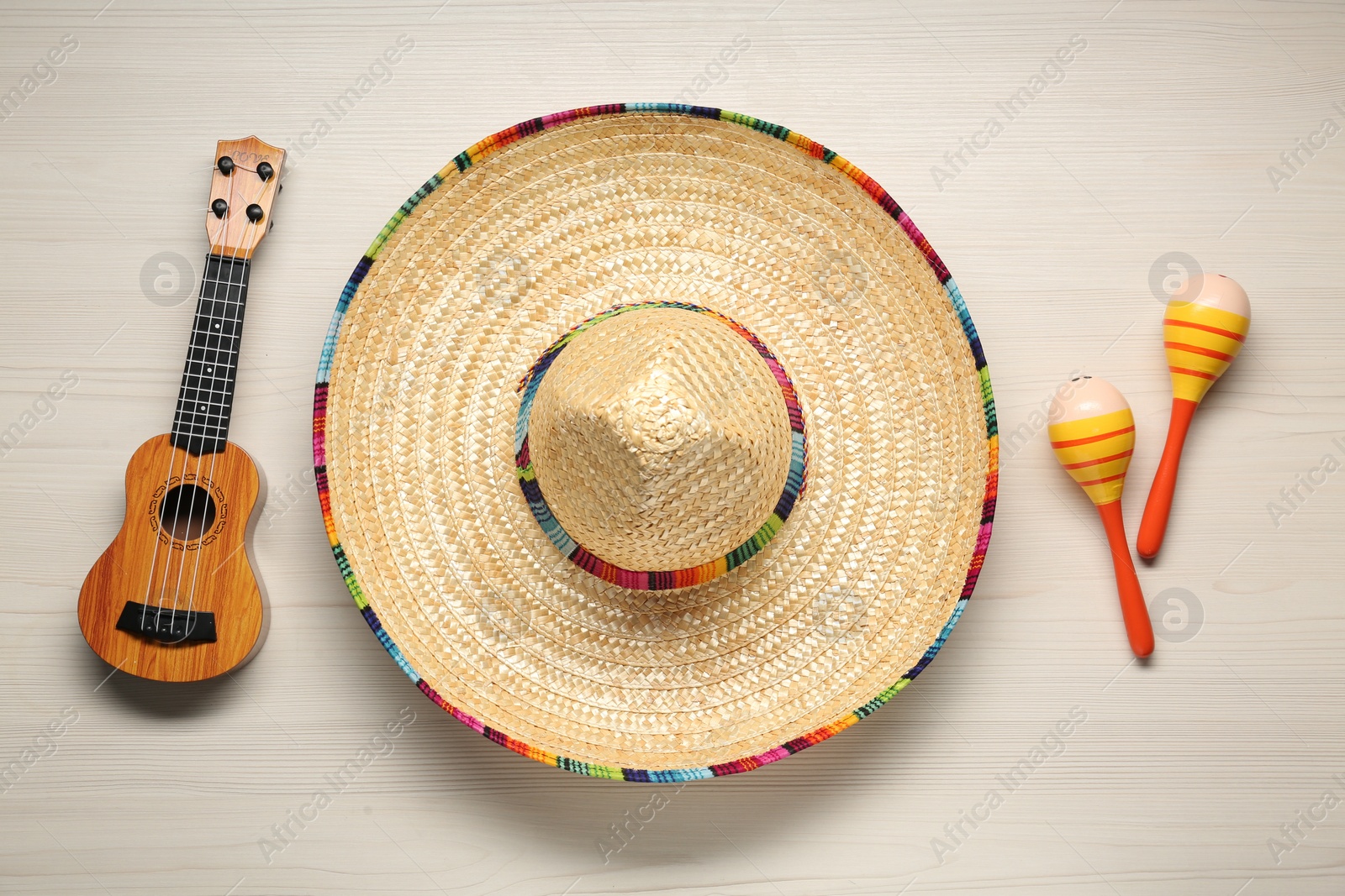 Photo of Mexican sombrero hat, maracas and guitar on white wooden background, flat lay