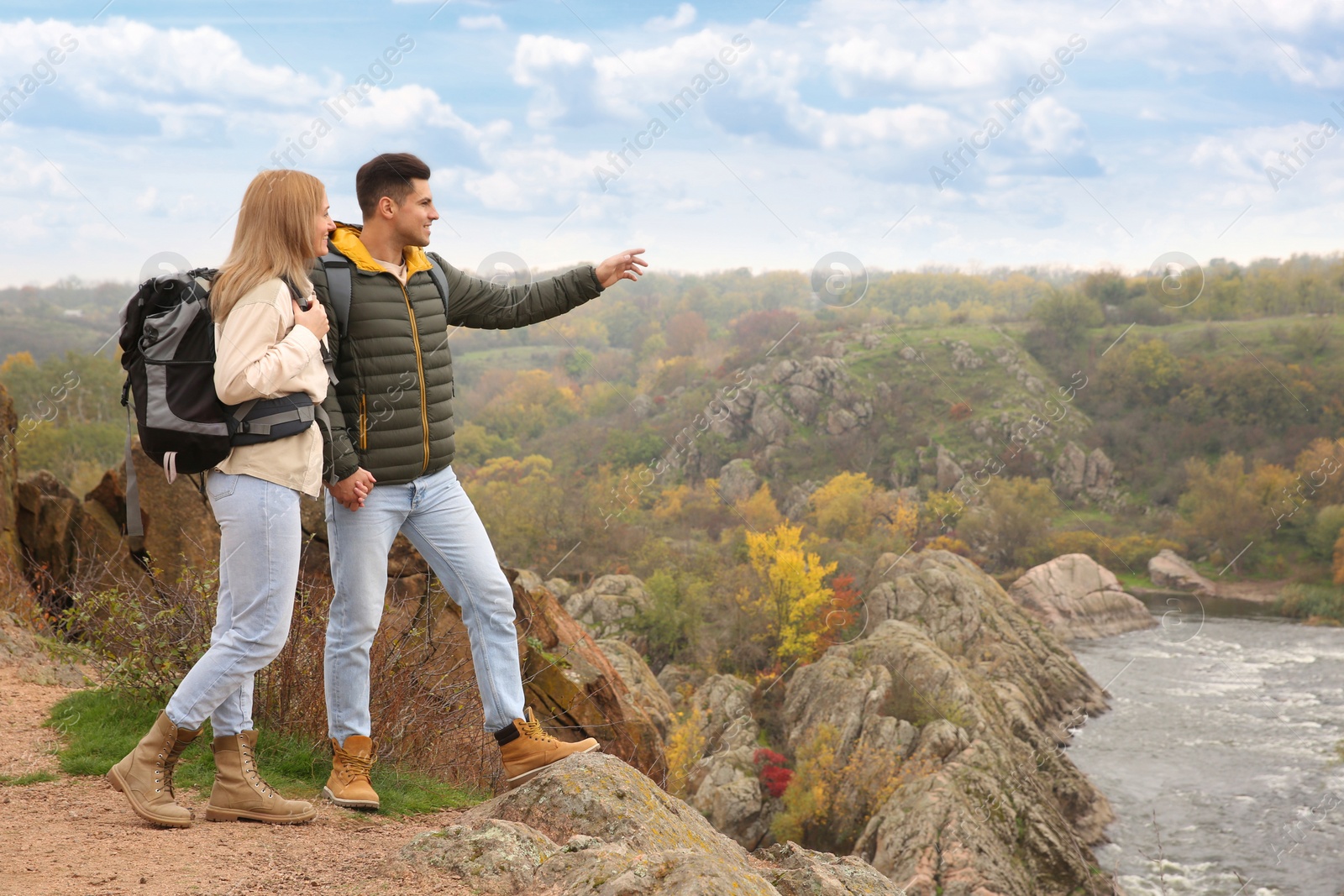 Photo of Couple of hikers with travel backpacks enjoying beautiful view near mountain river