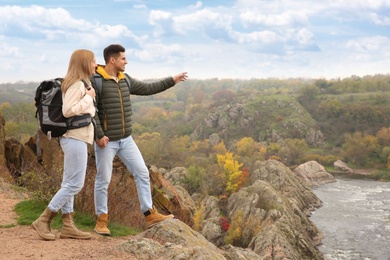 Photo of Couple of hikers with travel backpacks enjoying beautiful view near mountain river