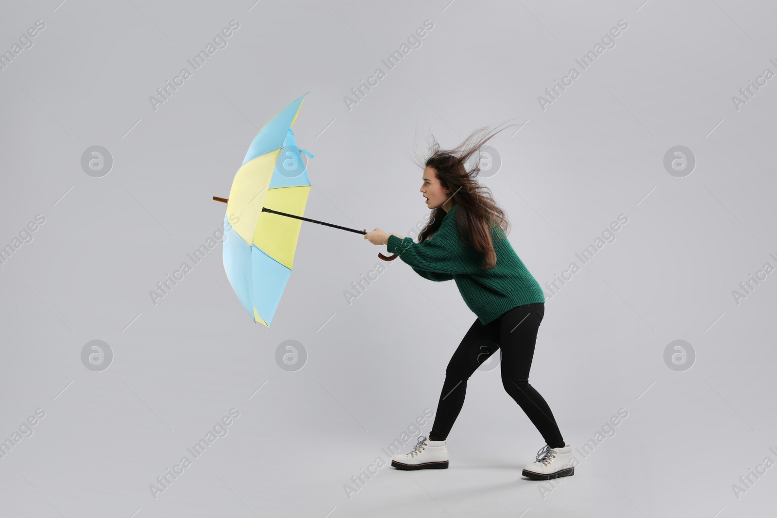 Photo of Emotional woman with umbrella caught in gust of wind on grey background