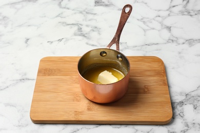 Photo of Saucepan with melting butter on marble table