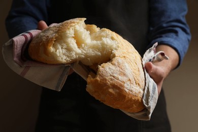 Photo of Man breaking loaf of fresh bread on dark background, closeup