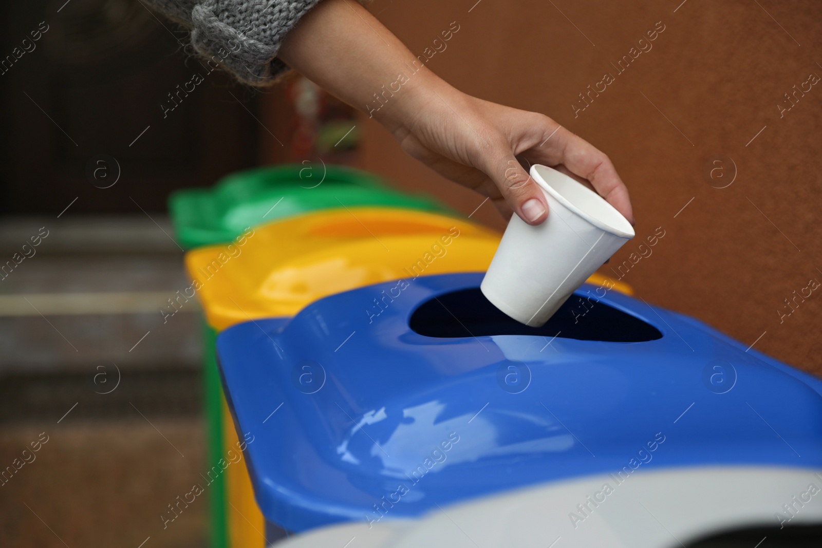 Photo of Woman throwing coffee cup into recycling bin outdoors, closeup