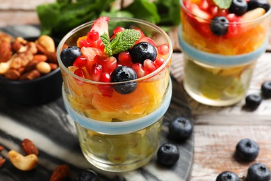 Photo of Delicious fruit salad, fresh berries, mint and nuts on wooden table