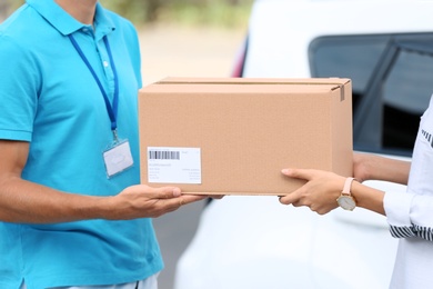 Photo of Young woman receiving parcel from courier outdoors