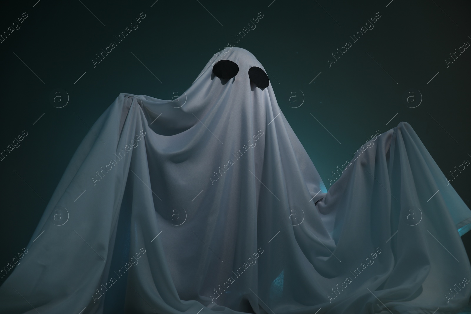 Photo of Creepy ghost. Woman covered with sheet on dark teal background, low angle view