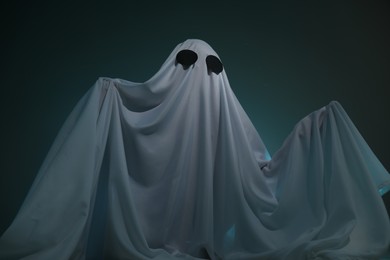 Photo of Creepy ghost. Woman covered with sheet on dark teal background, low angle view