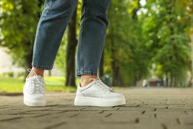 Woman in stylish sneakers walking on city street, closeup