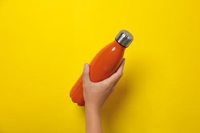 Woman holding modern orange thermos on yellow background, closeup